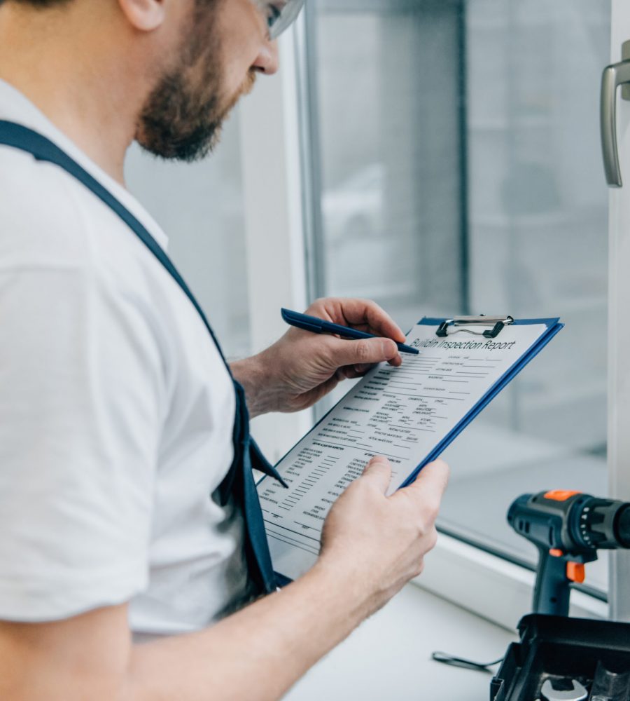 cropped shot of male handyman writing in clipboard and checking window